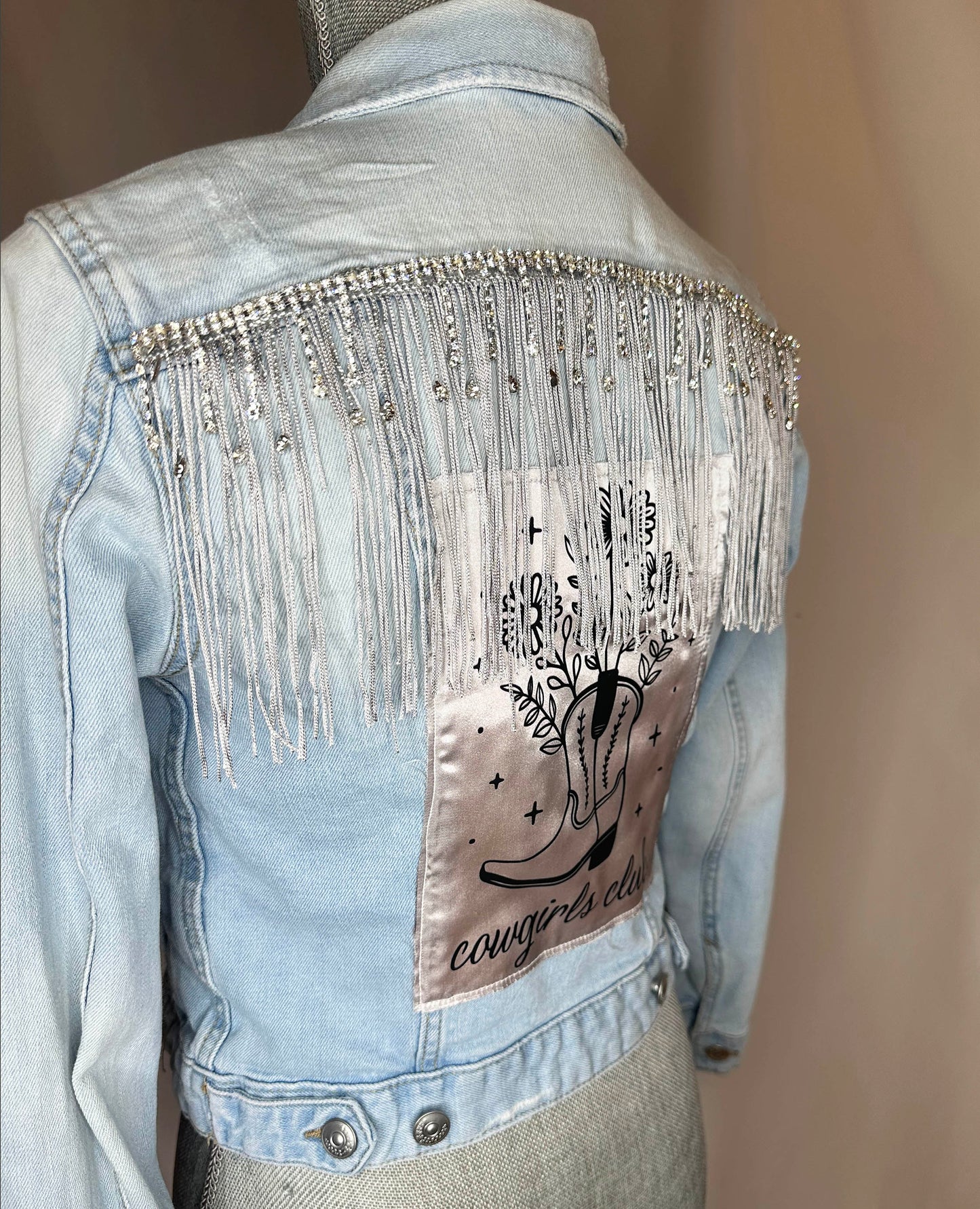 Fringe "Cowgirl club" Womens Light Denim Jacket Back Side Angle. Silver rhinestone detailing with silver fringe and satin patch.