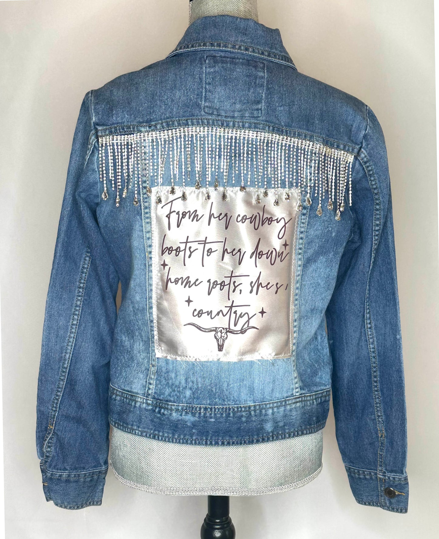 "From her cowboy roots" Womens Denim Jacket back side featuring rhinestone fringe detailing and satin patch.