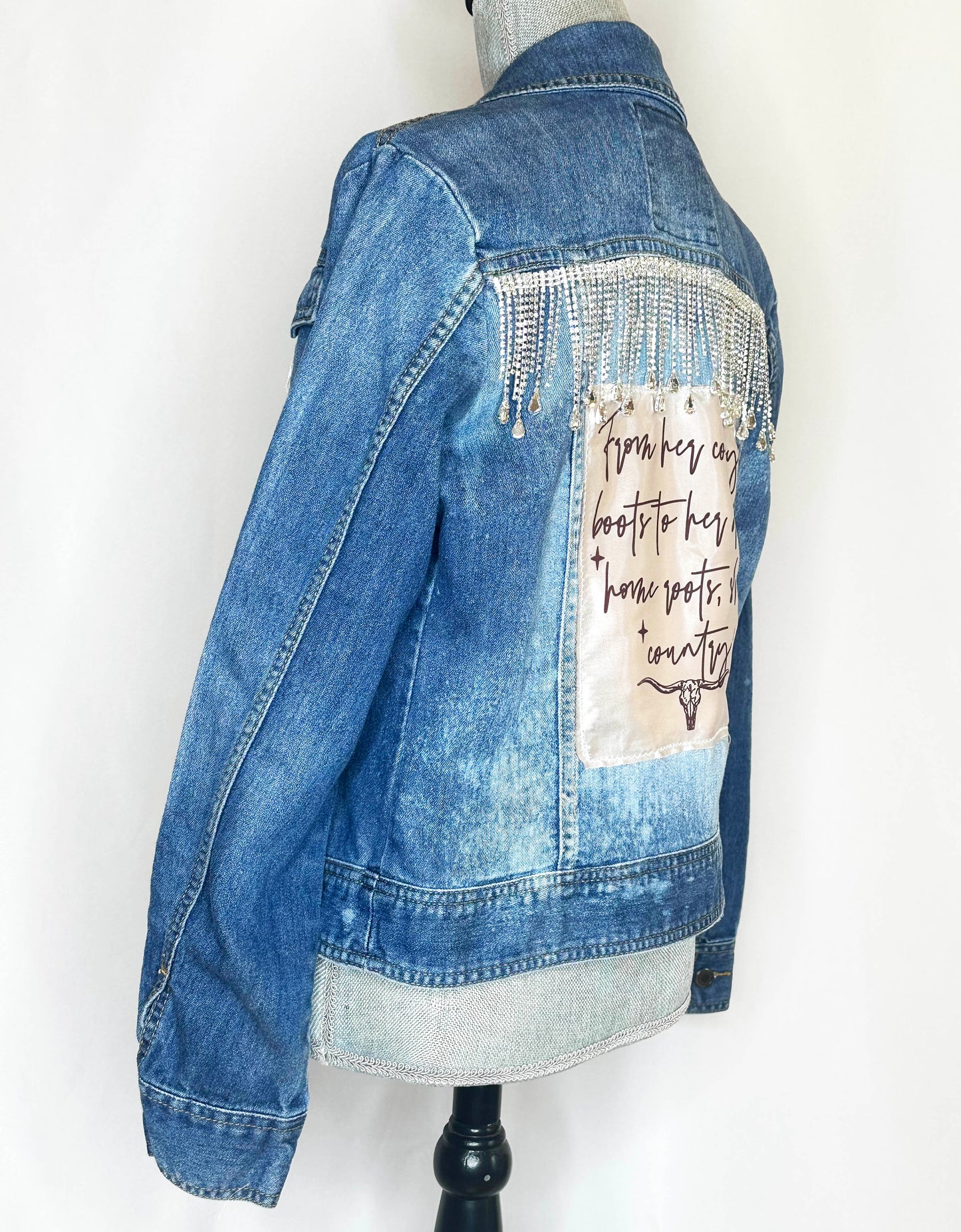 "From her cowboy roots" Womens Denim Jacket Side featuring rhinestone fringe detailing, satin patch and seamless stitching.