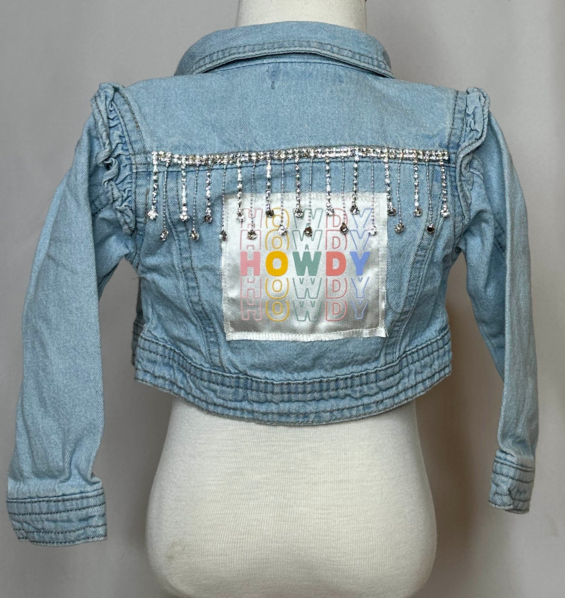 "Howdy" Fringed Toddler Denim Jacket Back Side with Ruffled shoulder cuffs and rhinestone trim detailing. 