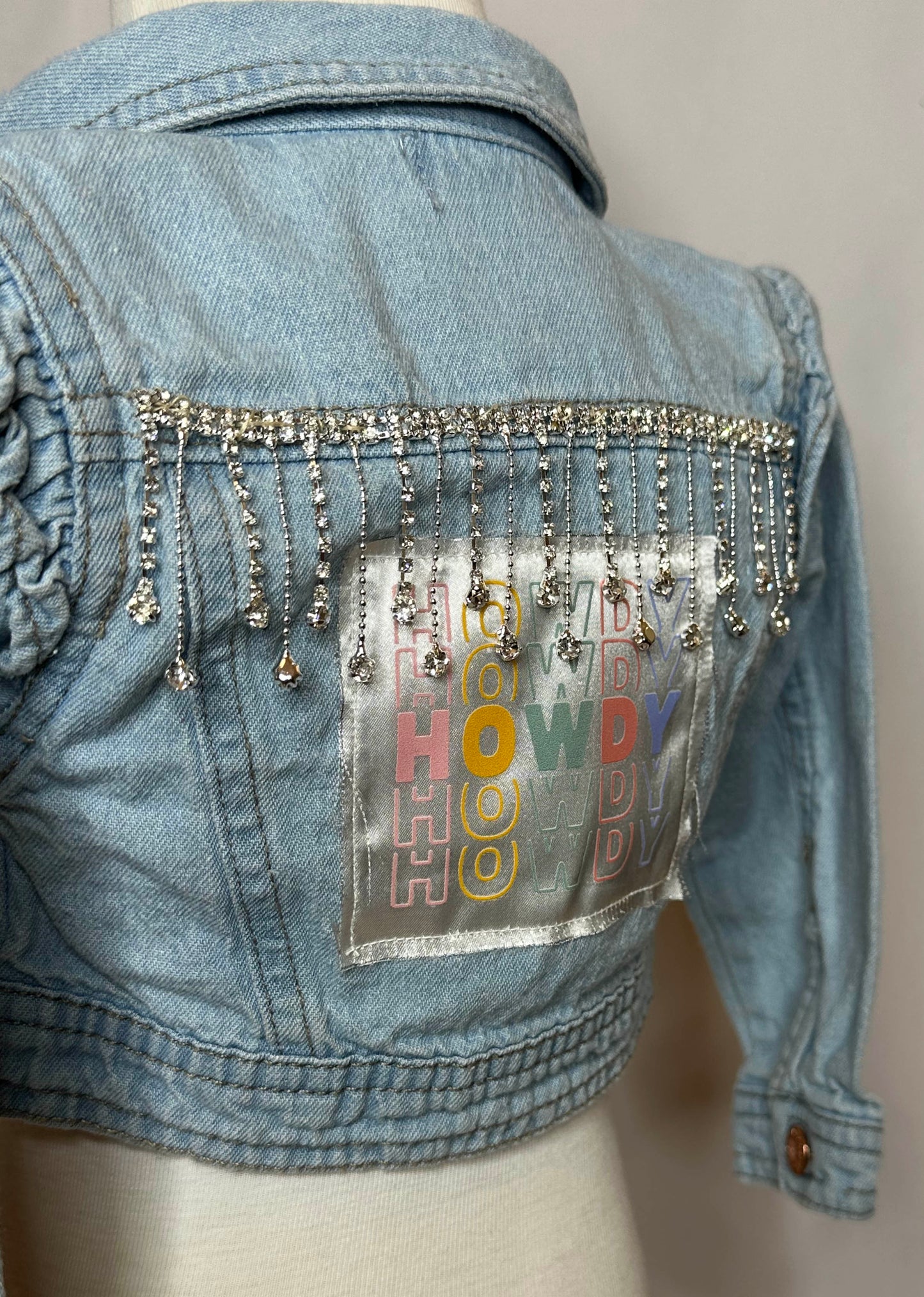 "Howdy" Fringed Toddler Denim Jacket Back Side close up with Ruffled shoulder cuffs and rhinestone trim detailing. 