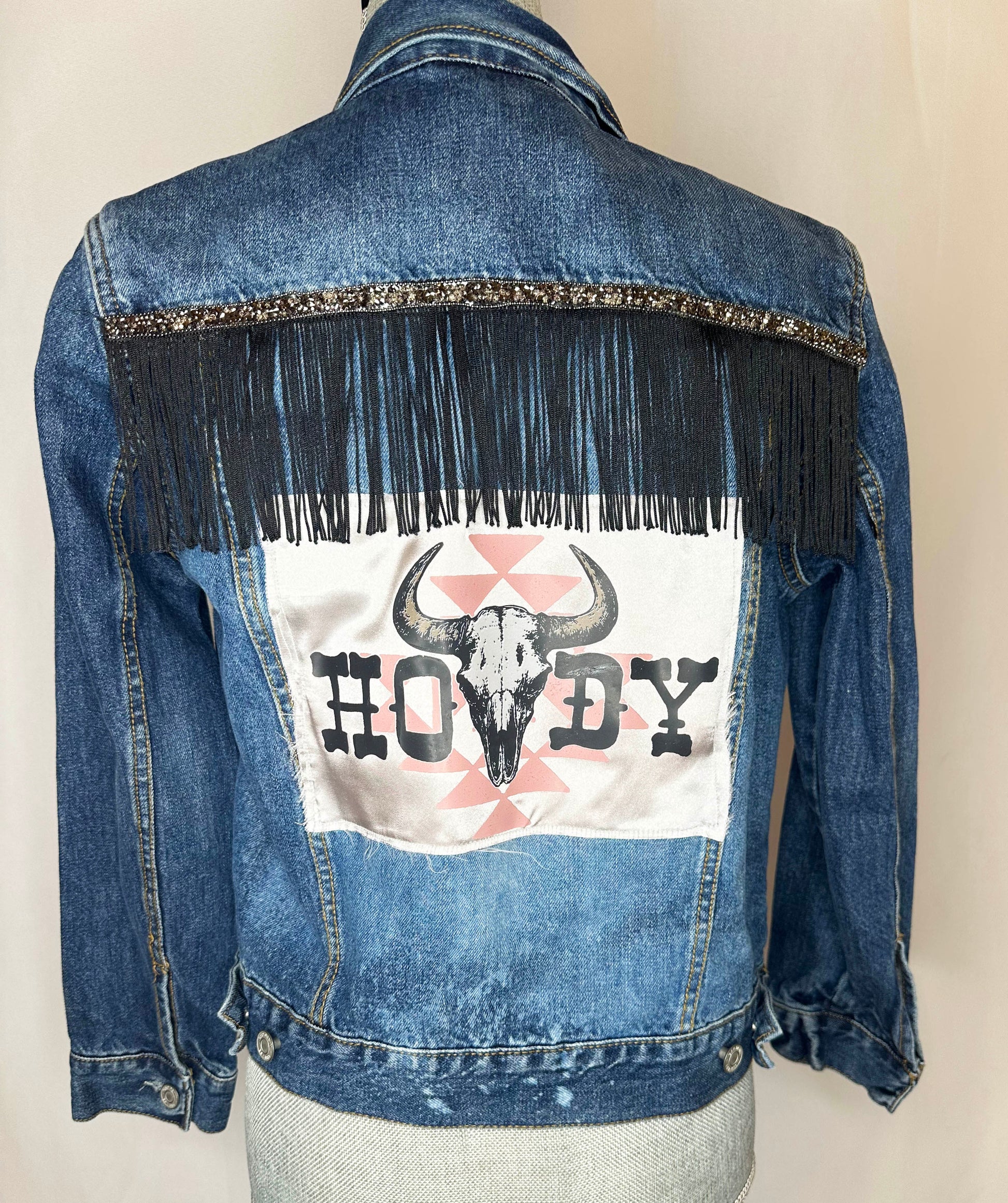 "Howdy" Women's Fringe Denim Jacket Back Side featuring rhinestone trim and black fringe detailing with satin patch.