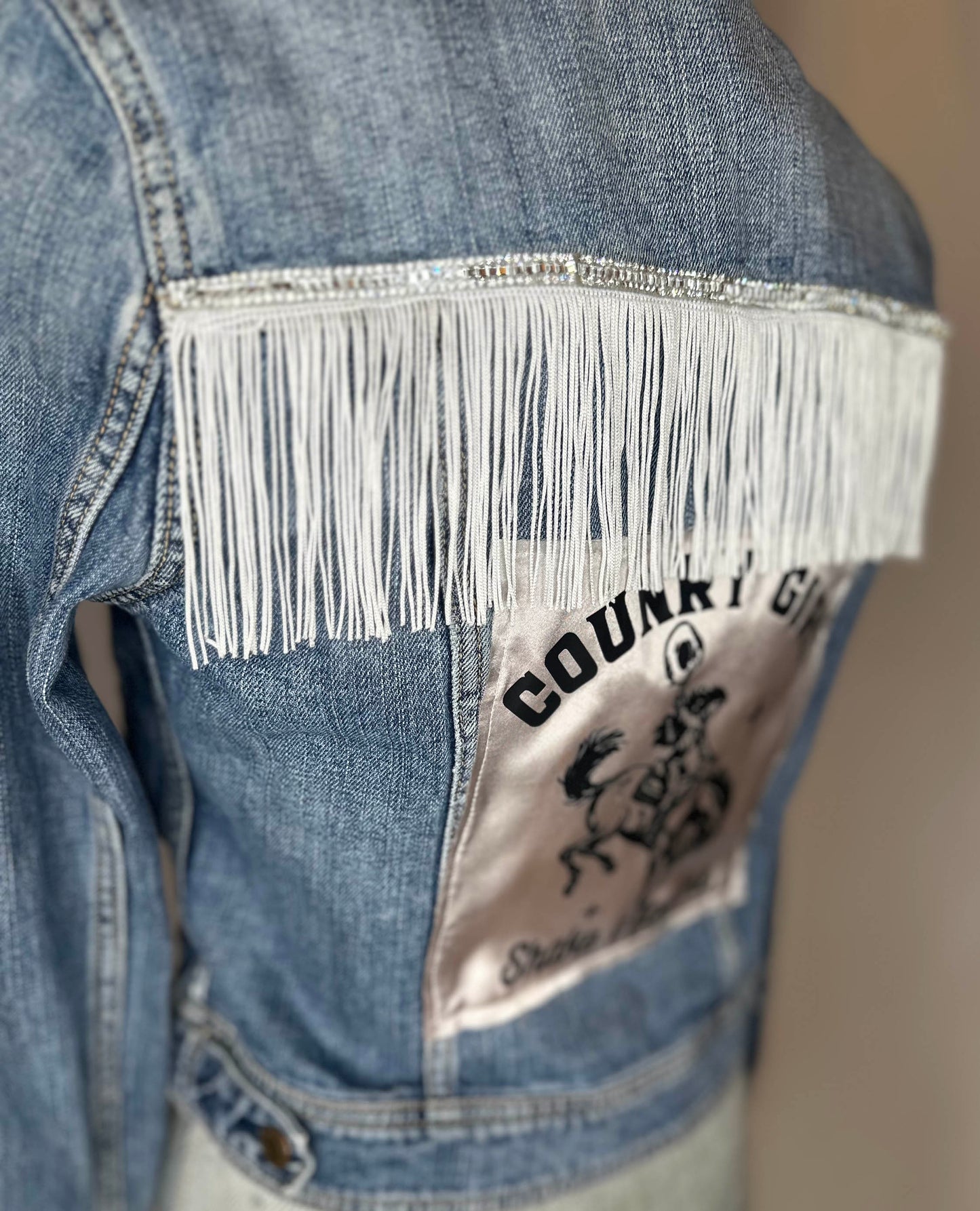 White Fringe "Country girl shake it for me"  Womens Denim Jacket Back Side View with rhinestone, white fringe and satin detailing.